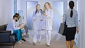 In the modern hospital corridor the main doctor female explain using a digital tablet to her colleague the diagnostic of