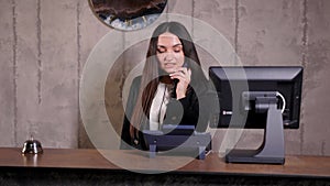 Modern hotel reception desk with bell. Happy female receptionist worker standing at hotel counter and talking to phone