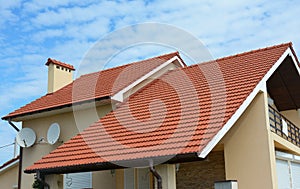 Modern house with chimney, red clay tiled roof and gable and valley type of roof construction. Building attic house construction
