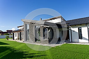 Modern house with gray stone wall and white walls in a garden witg fresh green gras