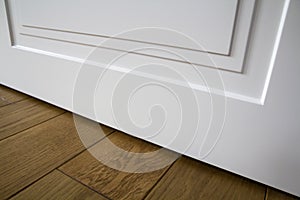Modern house interior detail with wooden parquet floor and white door. Apartment after renovation close-up.