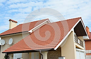 Modern house with red clay tiled rooftop, balcony, roof gutters, chimney. Valley and gable type of roof