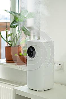 Modern humidifier at home, moistens dry air surrounded by indoor plant. Humidification concept