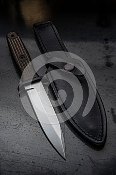 A modern hunting knife and a leather case for him on a dark background. Melee weapons for hunting and self-defense. The instrument