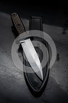 A modern hunting knife and a leather case for him on a dark background. Melee weapons for hunting and self-defense. The instrument