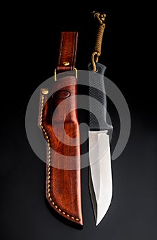 A modern hunting knife and a leather case for him on a dark background. Melee weapons for hunting and self-defense. The instrument