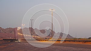 Modern illuminated highway with car in desert on sand mountain background.
