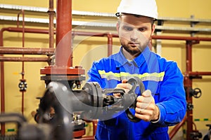 Modern industrial machine operator working in heating station. Worker turns gate valve of pipeline. Man in workwear closes valve