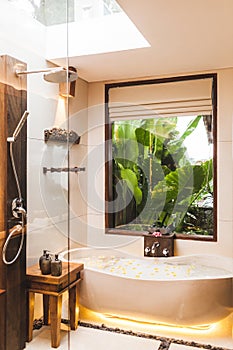 Modern interior of bathroom with bathtub and tropical garden view through window