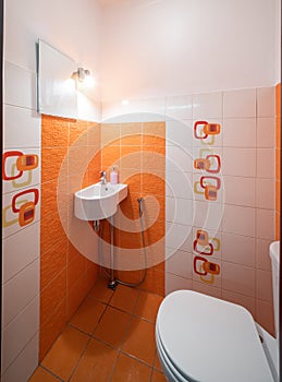 Modern interior of bathroom. Orange tile. Sink and toilet.