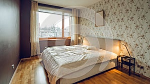 Modern interior of bedroom in luxury apartment. Cozy bed. Huge window. Lamps on nightstands.