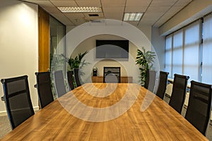 Modern interior of boardroom, meeting or seminar room with chairs and long wooden table at workplace or office, green plants and T