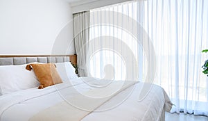 Modern interior cozy bed near a window with white curtains in bedroom. pillows and white soft blanket for rest and sleep