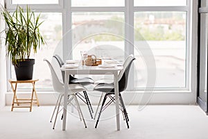 Modern interior of a cozy dining room kitchen, white furniture, against the background of a panoramic window. Conceptual decor