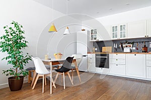 Modern interior of cozy kitchen, dining room, white furniture, wall, black accessories, natural materials, wooden chairs