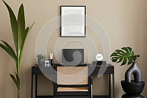 Modern interior design of home office space with stylish chair, desk, commode, black mock up poster frame, laptop, book, desk.