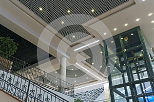 Modern interior design inside the mall. Glass transparent elevator in the business center. View of the ceiling, moldings and LED