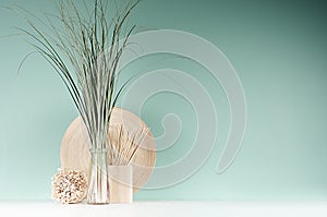 Modern interior in farmhouse style - bamboo plate, sheaf of cane in glass bottle, decorative round sheaf of twigs, sticks on green