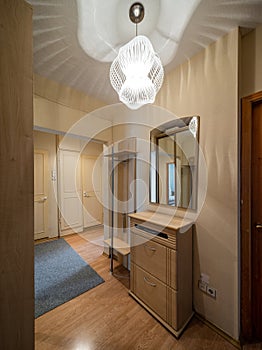 Modern interior of hall in apartment. Wooden door. Mirror and stand with drawers.