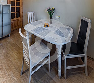 Modern interior of kitchen. White table and chairs. Flowers and fruits. Wooden door.