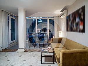 Modern interior of living room in luxury private house. Cozy sofa. Served table and chairs. Panorama windows.