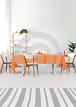 Modern interior. Long dining room table with chairs. White walls and floor, orange details. Real photo concept