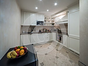 Modern interior of private house. Light spacious kitchen. Fresh fruits in plate.