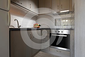 Modern interior of small corner kitchen with white subway brick tile splashback. Fruit plate on light wooden cabinets background