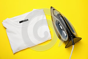 Modern iron and folded t-shirt on yellow background, top view