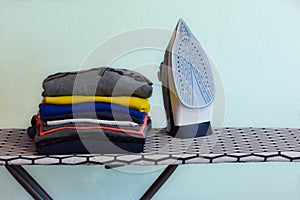 Modern iron on ironing board and a pile of clean and tidy clothes