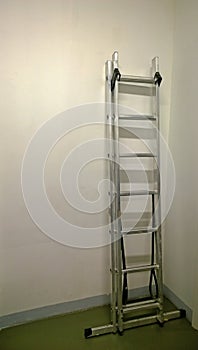 Modern iron ladder leaning against a white wall in the assembled condition during repair in apartment or office