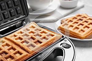 Modern iron with tasty Belgian waffles on table, closeup