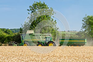 Modern John Deere combine harvester cutting crops with tractor and trailer