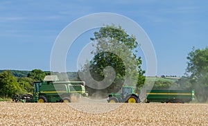 Modern John Deere combine harvester cutting crops with tractor and trailer