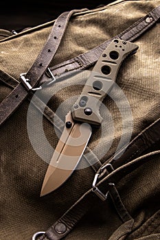 Modern khaki folding knife on a rough canvas backpack