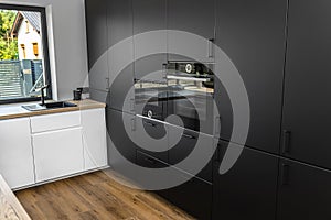 Modern kitchen with black fronts, built in oven and microwave, vinyl panels on the floor.