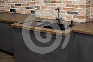 Modern kitchen with black sink, kitchen faucet for water and fronts against the background of a brick wal