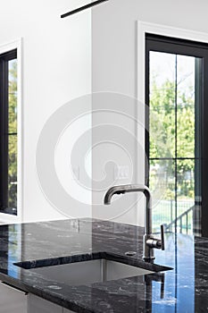 A modern kitchen detail with a black stainless faucet and black marble countertop.