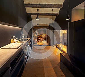 Modern kitchen front view in a renovated mountain chalet. At the back there is the pantry with hanging salami and ham and some