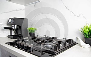 Modern kitchen with gas hob against white granite tiles. Decoration pots with artificial flowers. Copy space for text photo