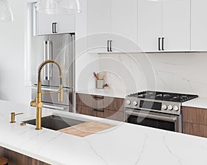 A modern kitchen with a gold faucet and white and wood cabinets.