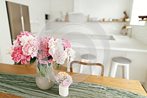 Modern kitchen interior. Beautiful peonies in vase on wooden table on background of stylish white kitchen with appliances in new