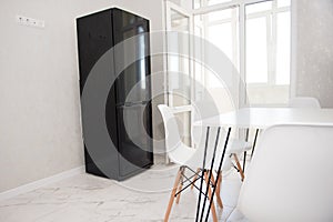 Modern kitchen interior with white dining table, white chairs and black refrigerator. Modern design, dining table and chairs in