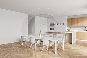 Modern kitchen interior with white walls  a wooden parquet floor and white countertops. A long table with chairs near it. Mock up