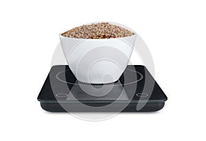 Modern kitchen scale with bowl of raw buckwheat isolated on white