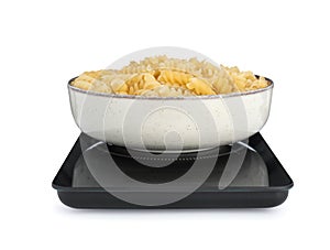 Modern kitchen scale with bowl of raw pasta isolated on white