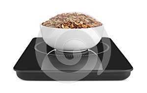 Modern kitchen scale with bowl of tasty granola isolated on white