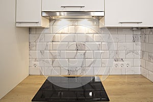 Modern kitchen view with empty induction cooker hob in wooden counter and white tile backsplash and cabinets