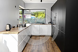 A modern kitchen with white and black fronts and a large corner window, vinyl panels on the floor.