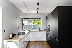 A modern kitchen with white and black fronts and a large corner window, vinyl panels on the floor.